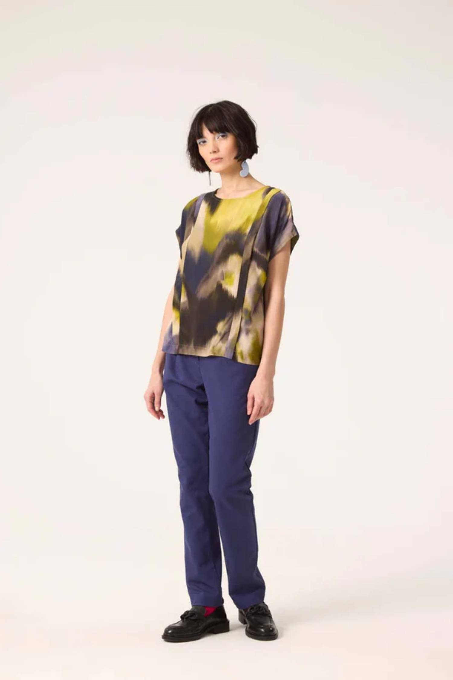 A woman wearing the Fuzzy Top by Cokluch in Vertigo print with blue pants, standing in front of a white background 