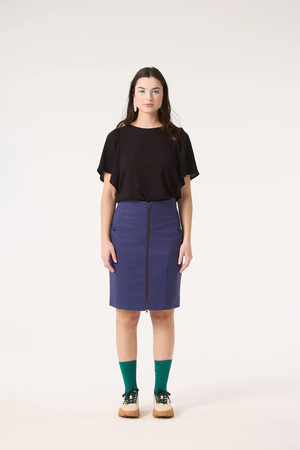 A woman wearing the Divine Top by Cokluch in Black, featuring a round neck and short ruffled sleeves, with a blue skirt. 