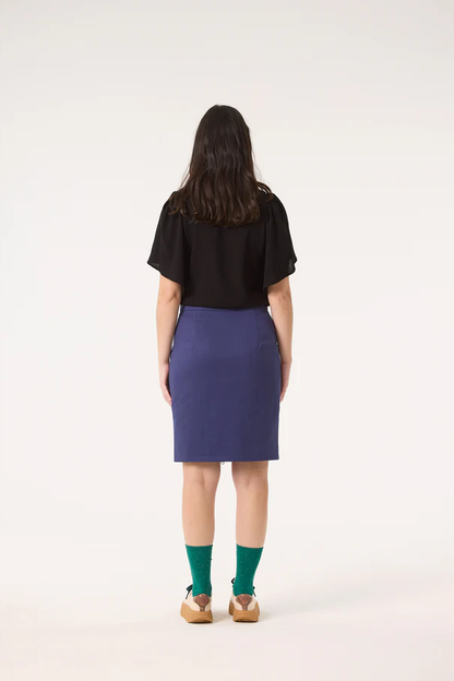 Back view of a woman wearing the Divine Top by Cokluch in Black, featuring a round neck and short ruffled sleeves, with a blue skirt. 