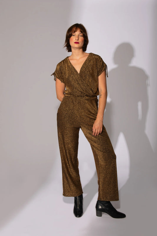 A woman wearing the Eve Lavoie Last Night jumpsuit in Gold, standing in front of a white background 