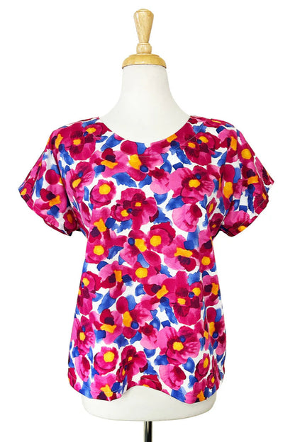 The Macaron Top by Desserts and Skirts in Pink Floral, with a round neck, short sleeves, and a loose fit, is shown on a mannequin against a white background. 