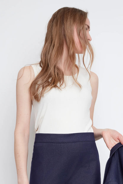 Close up of a woman wearing the Lucille Tank by Julei in Natural White, a ribbed tank with a round neck. She is wearing it with denim pants and holding a denim jacket in her hand. 