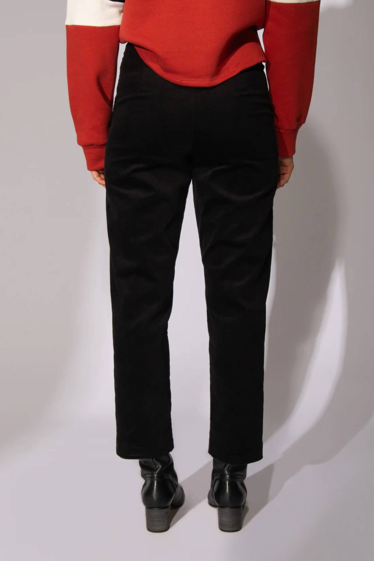 Waist down back view of a woman wearing the Comin' Through Corduroy Pants by Eve Lavoie in Black, with the Sour Time crewneck in Terracotta