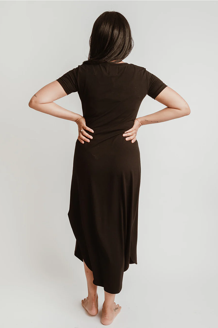 Back view of a woman wearing the Field Dress by Blondie Apparel in Black, standing in front of a white background