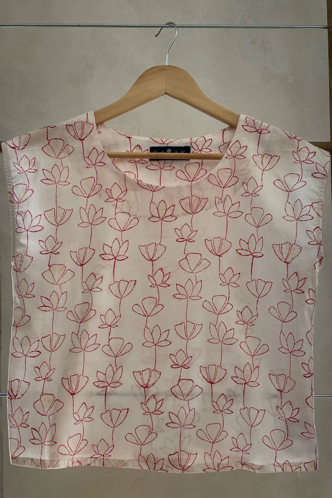The Sandrigo Top from Kazak in Red Floral print, a cotton top with short extended sleeves and a wide round neck, is shown on a wooden hanger against a grey background. 