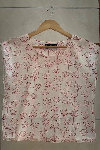 The Sandrigo Top from Kazak in Red Floral print, a cotton top with short extended sleeves and a wide round neck, is shown on a wooden hanger against a grey background. 