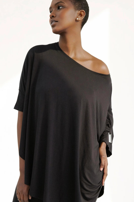 A woman wearing the Flo Oversized Bamboo Tee by Stacey Martin Lifestyle in Black. She is wearing it with black leggings and standing in front of a white background