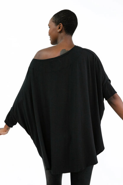Back view of a woman wearing the Flo Oversized Bamboo Tee by Stacey Martin Lifestyle in Black. She is wearing it with black leggings and standing in front of a white background