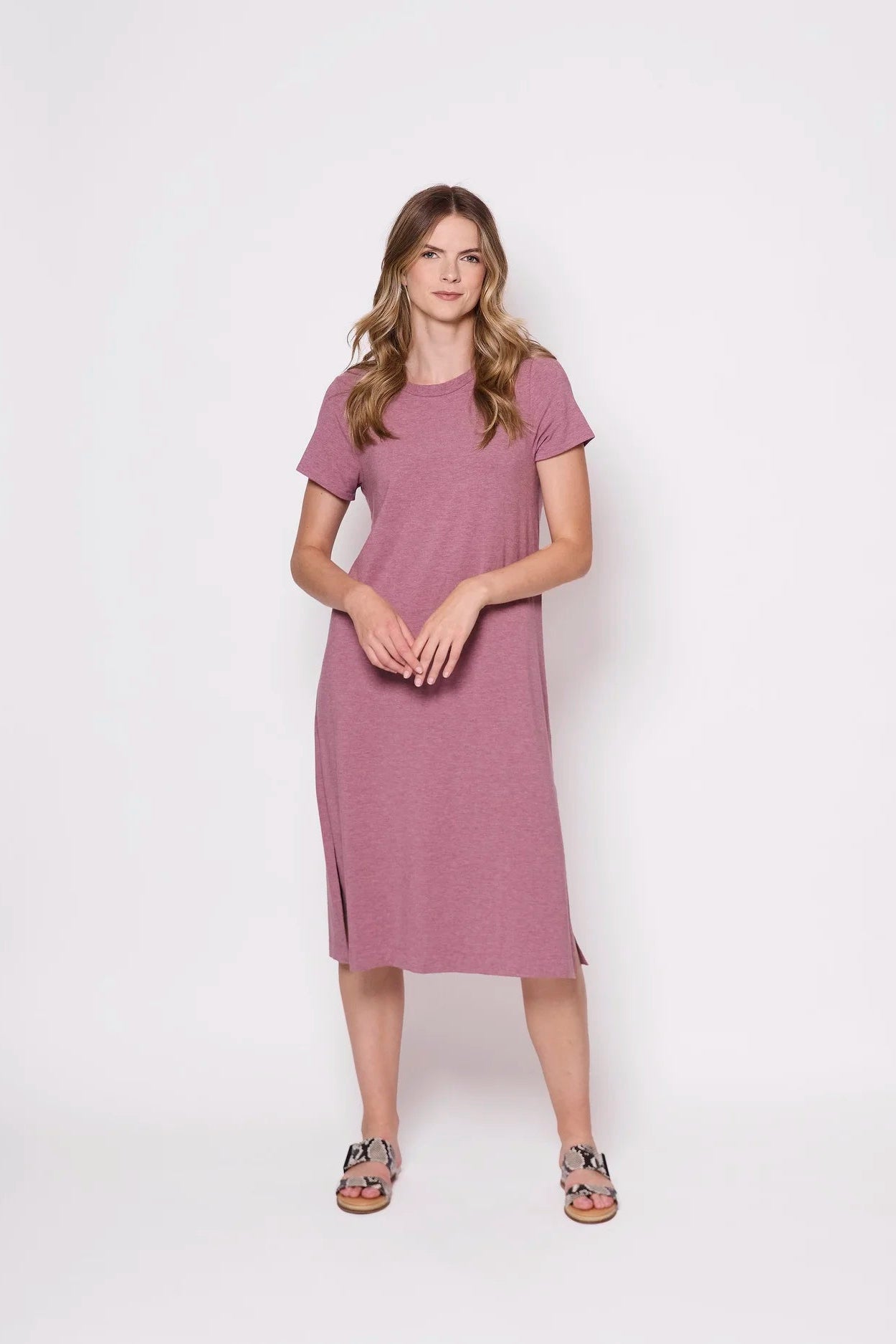 A woman wearing the Frances Midi  by Tangente in Heather Rose, short sleeved loose fitting dress with side slits. She is  standing against a plain background