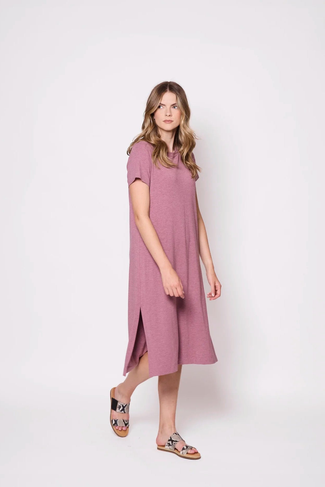 A woman wearing the Frances Midi  by Tangente in Heather Rose,  a short sleeved loose fitting dress with side slits. She is standing against a plain background