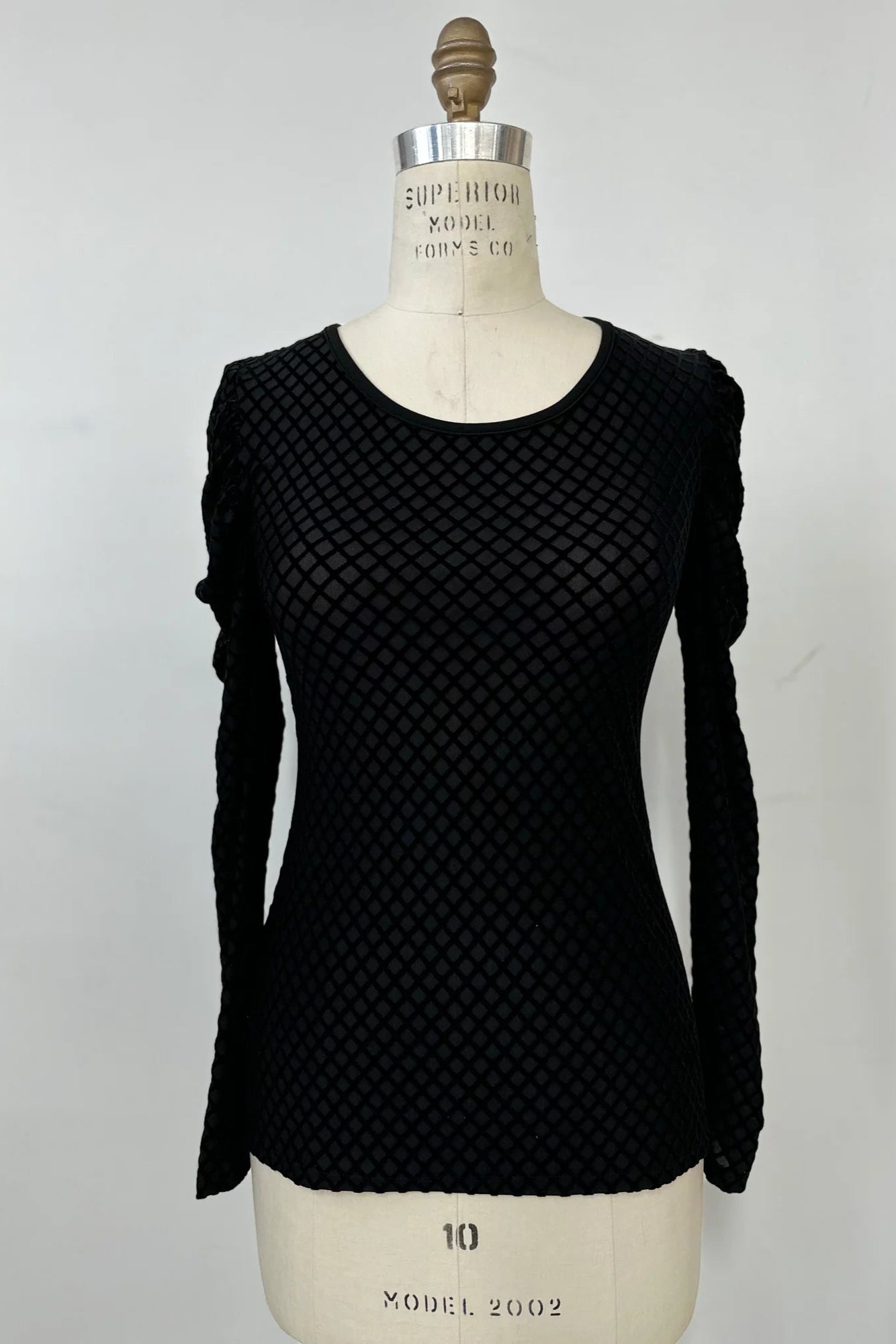 The Octavia Sweater by Kollontai, featuring black cut velvet in a diamond pattern, gathered shoulders, long sleeves, an oval neckline, and a slim fit, is shown on mannequin against a white background. 