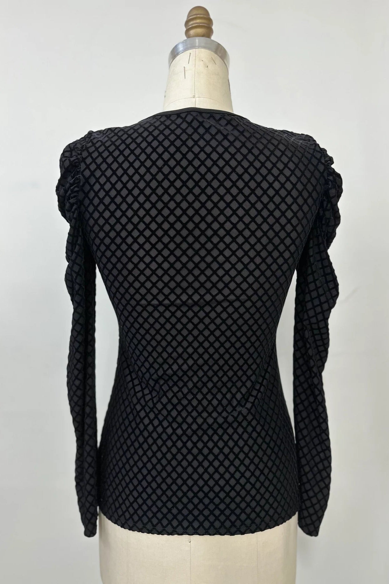A back view of the Octavia Sweater by Kollontai, featuring black cut velvet in a diamond pattern, gathered shoulders, long sleeves, an oval neckline, and a slim fit, is shown on mannequin against a white background. 