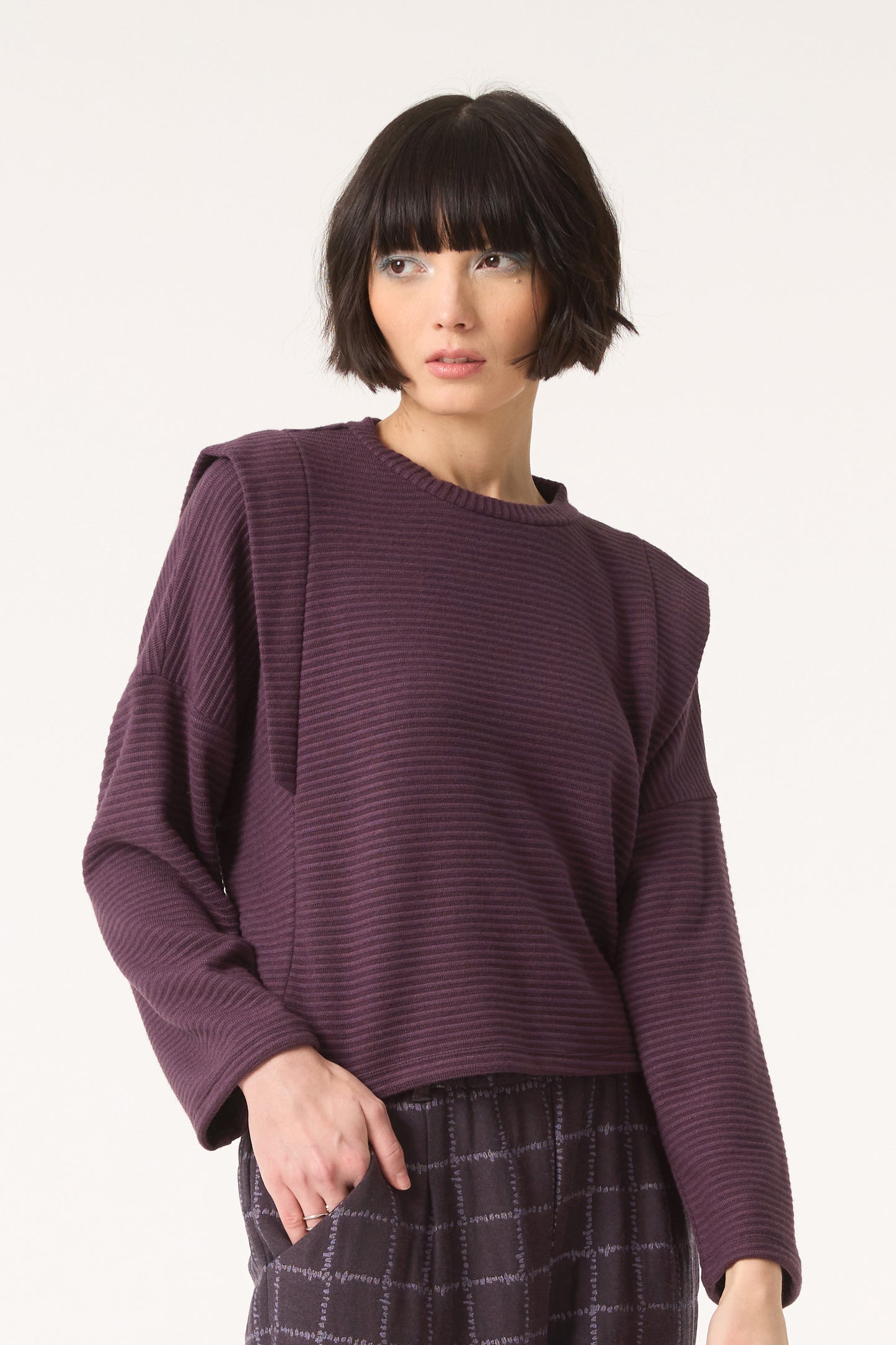 Semi close-up of a woman wearing the Galactic Sweater by Cokluch in Blackberry, standing in front of a white background