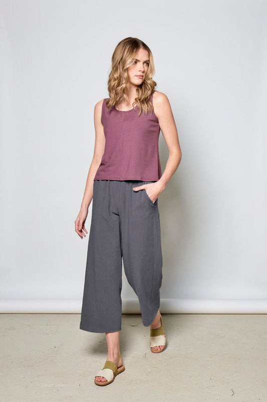 Woman wearing a purple sleeveless top and gray wide-leg pants against a white background