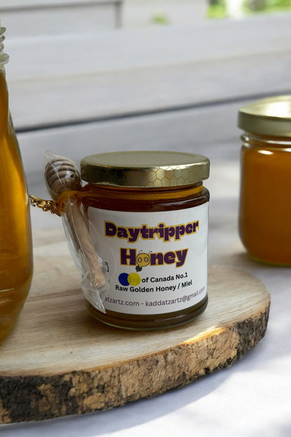 A jar of Daytripper Honey by Kaddatz is shown on a wooden cutting board in front of a tiled wall. 