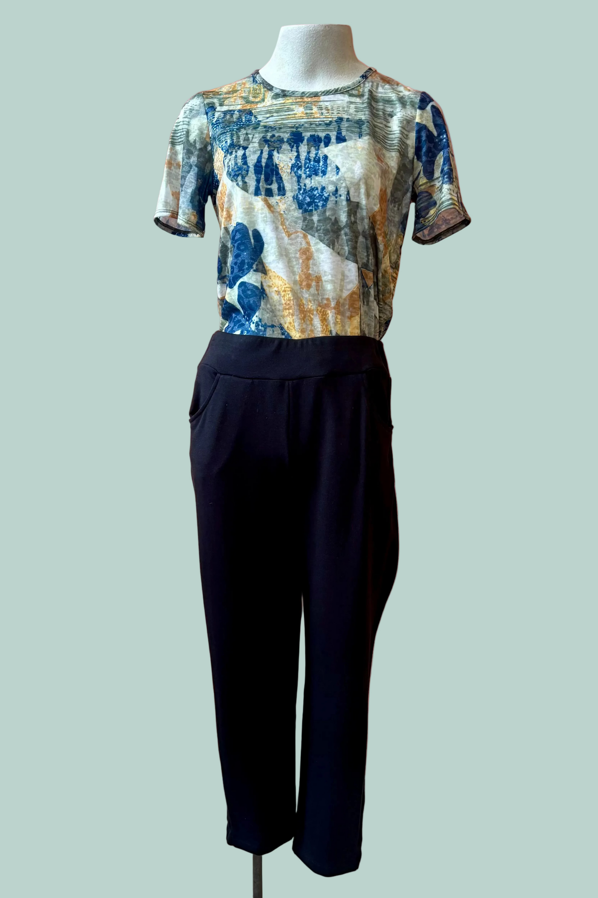 The Giselle Joggers by Pure Essence in Black are shown on a mannequin with a patterned shirt in front of a turquoise background. 