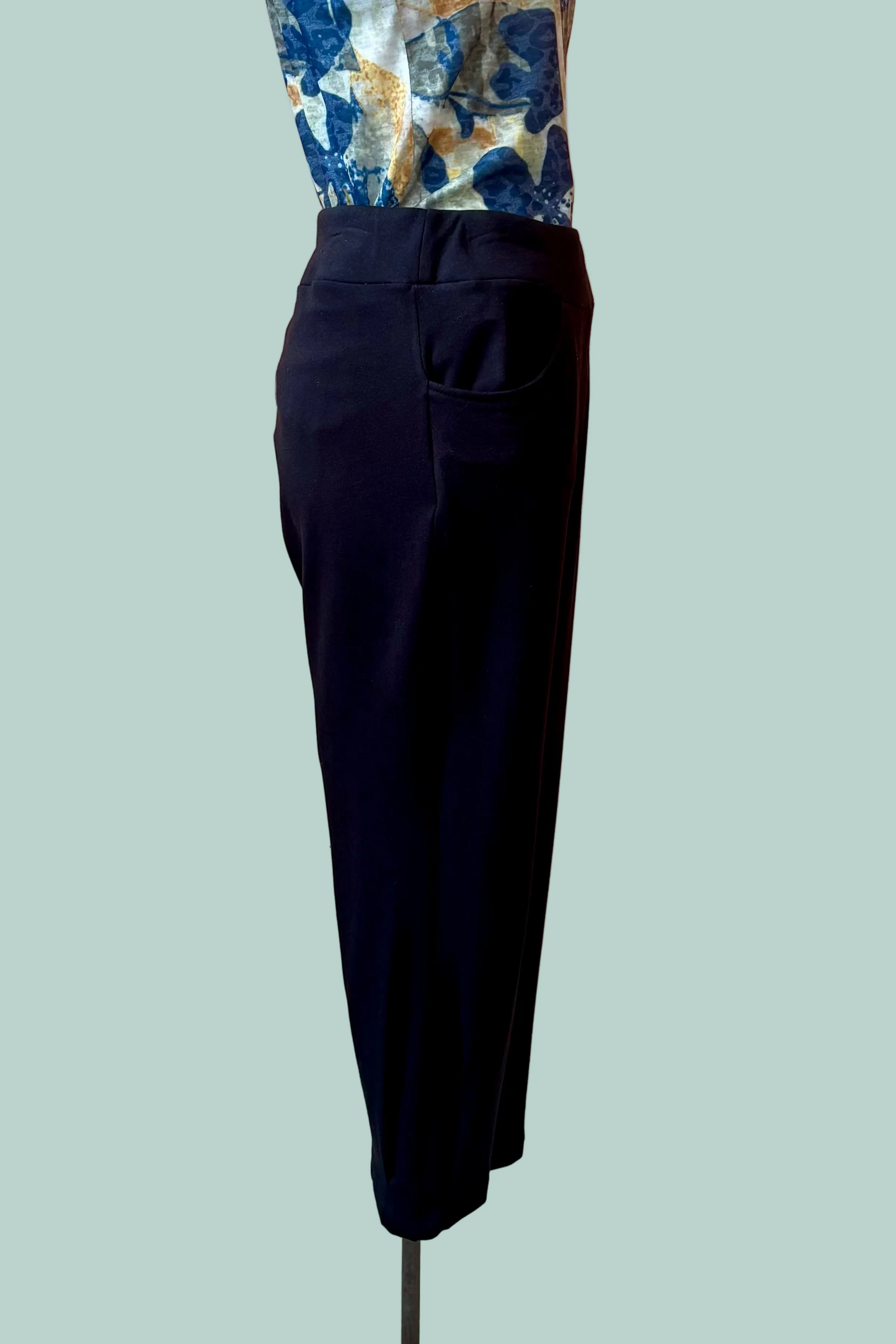 A side view of the Giselle Joggers by Pure Essence in Black are shown on a mannequin with a patterned shirt in front of a turquoise background. 