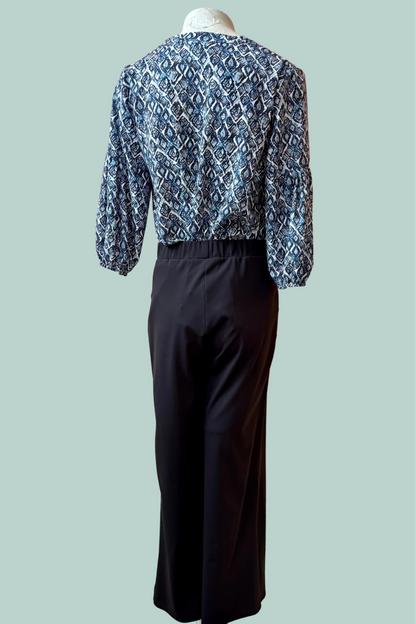 Back view of a mannequin wearing a the Gloria Pants by Pure Essence in Black with a blue patterned top on a light teal 