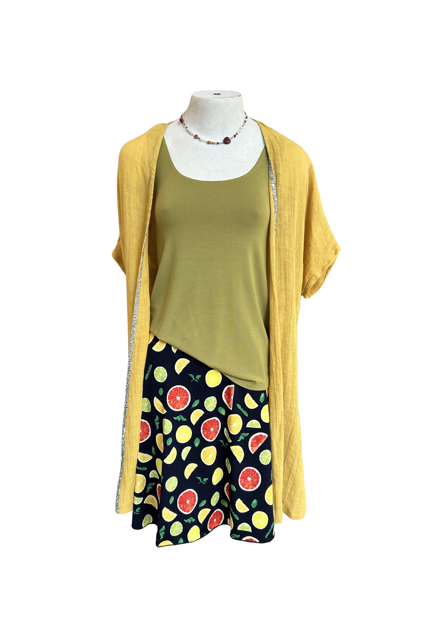 The Flirt Skirt by Slak in Citrus Print, an above the knee A-line skirt with a contrasting pull-on waistband, is shown on a mannequin with a green top and yellow cardigan against a white background. 