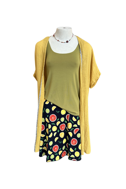 The Flirt Skirt by Slak in Citrus Print, an above the knee A-line skirt with a contrasting pull-on waistband, is shown on a mannequin with a green top and yellow cardigan against a white background. 