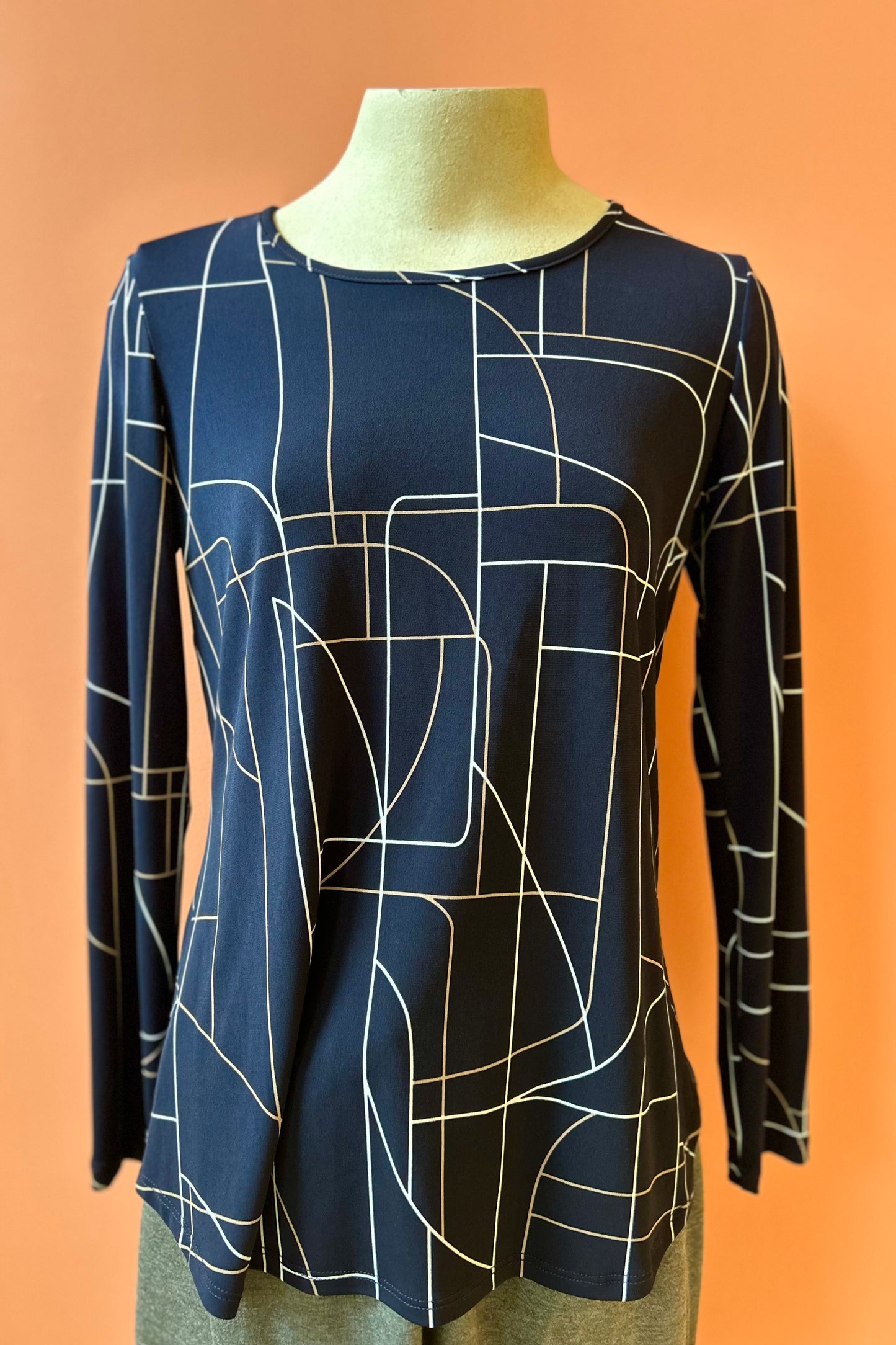 The Rain Top by Compli K in navy print is show on a mannequin in front of a coral background 