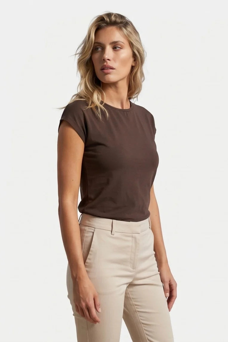 A woman wearing the Eowyn T-Shirt by Kollontai in Chocolate with tan pants standing against a grey background. 