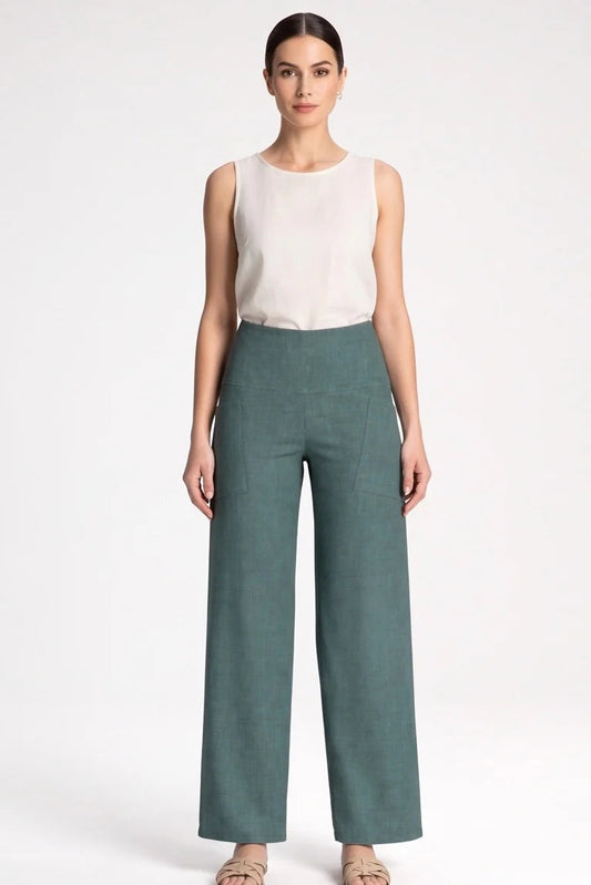 A woman wearing the Kollontai Susan Pants in Green with a white tank, standing in front of a grey background. 