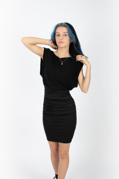 A woman wearing the Saki Top by Infime in glitter Black with a black skirt, standing in front of a white background 