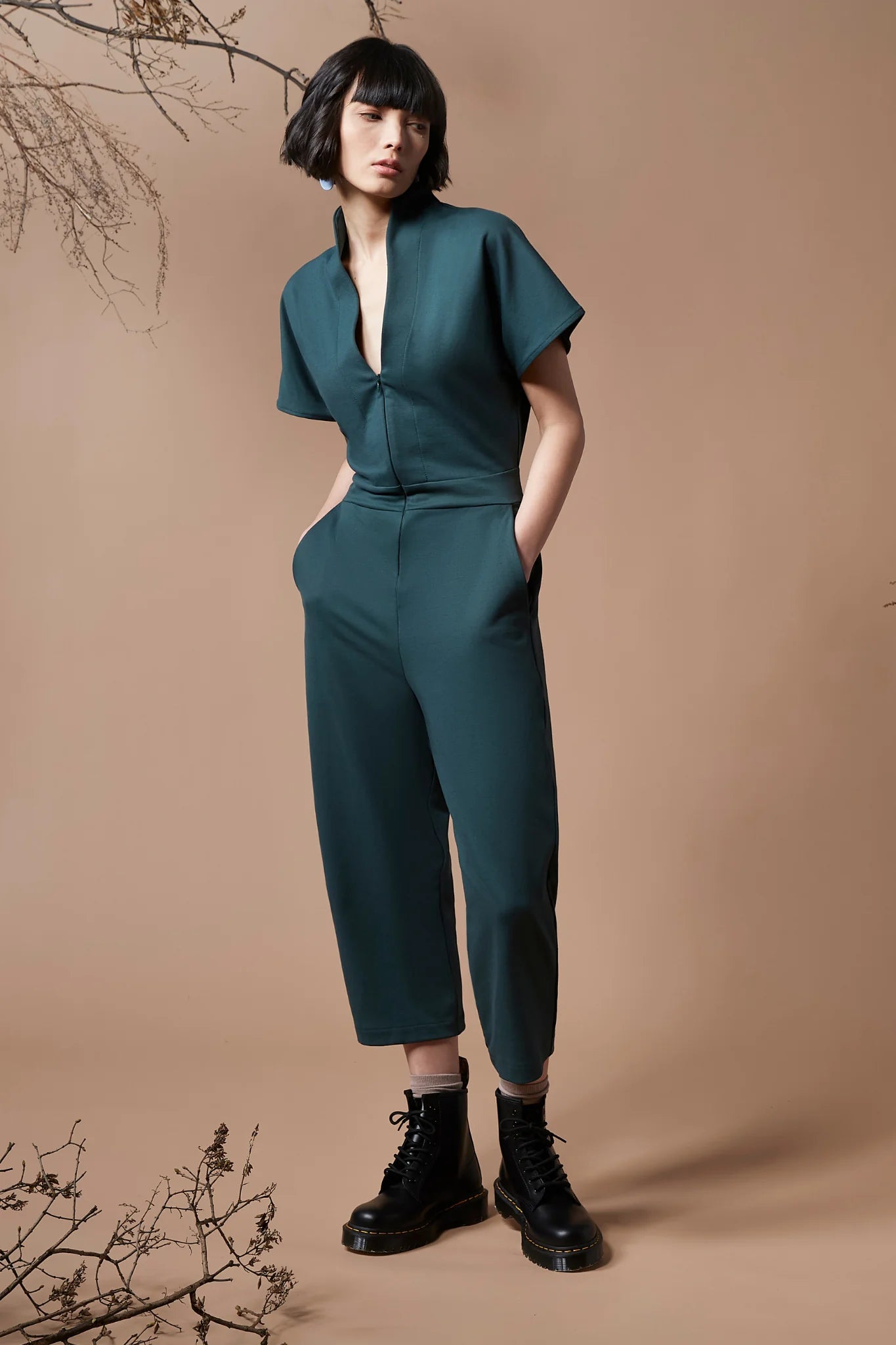 A woman wearing the Jayden Jumpsuit by Melow in Forest, standing in front of a beige background