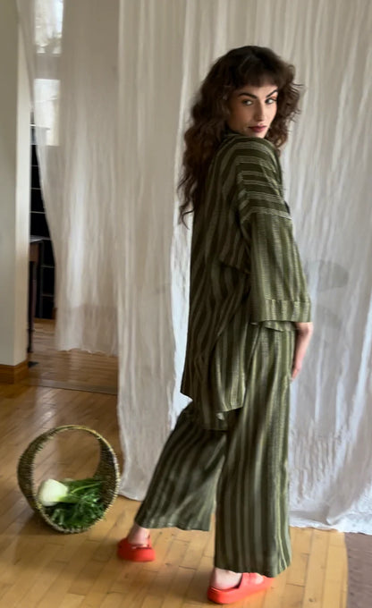 Side view of a woman wearing the Mirano Jacket by Kazak in Ivy Dots print, an open Kimono-inspired jacket that falls to mid-thigh and has wide 3/4 sleeves. She is wearing it with the matching Sienna Pants and is standing in front of a white curtain. 