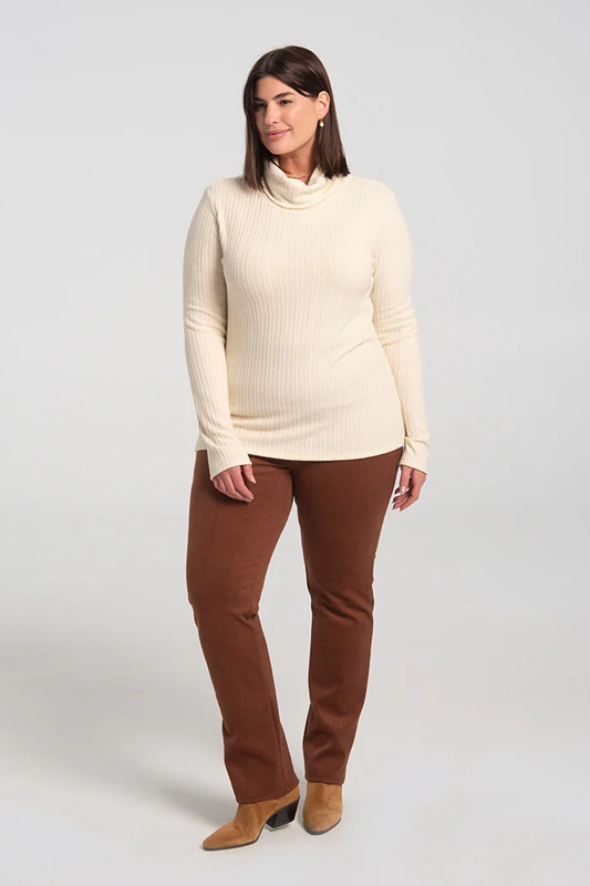 A woman wearing the Garfunkel Sweater by Kollontai in Cream with brown pants, standing in front of a white background 