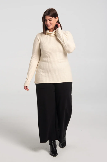A woman wearing the Garfunkel Sweater by Kollontai in Cream with black pants, standing in front of a white background 