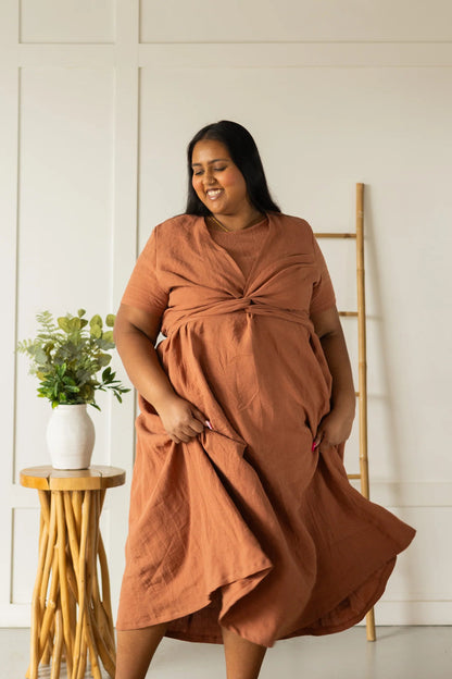 A woman wearing the Stella Top by Lights of All in Sedona, a short sleeved linen wrap top that can be twisted or tied back or front. She is wearing it over the matching Caroline dress and standing indoors by a plant stand. 