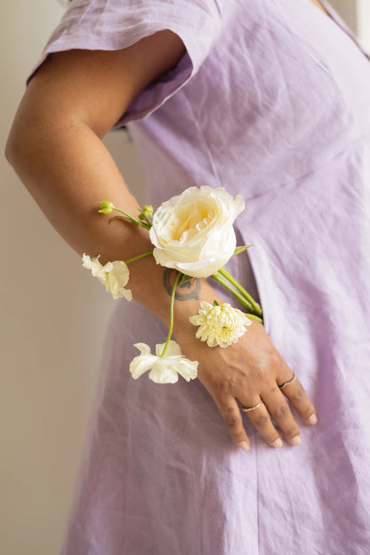 Close up of the pocket of the Emily Dress by Lights of All in Lavender, showing a woman's hand holding flowers. 