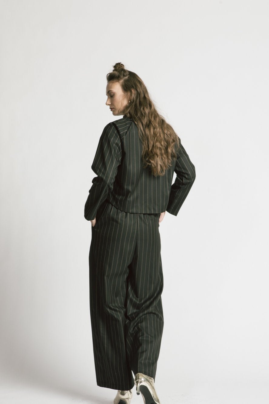 Back view of a woman wearing the Maurice Jacket by Allison Wonderland in pinstripe, with the Katherine Pant, standing in front of a white background 