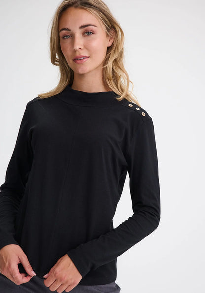 Waist up view of a woman wearing the Carleton Top by Message Factory in a Black, a long-sleeve top with button details on the shoulder. She is wearing it with grey bottoms and standing in front of a white background. 