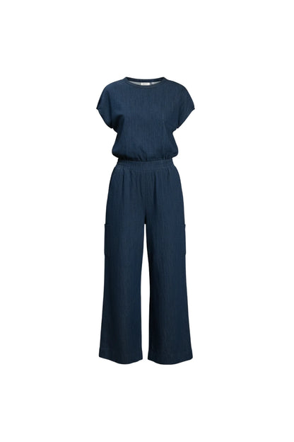 The Michele Jumpsuit by Melow in Denim, with short extended sleeves with gathered cuffs, a defined waist with elastic at the back and sides, an invisible back zip, a chest pocket, and wide full-length legs, is shown against a white background. 