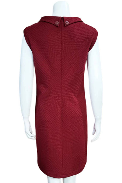 A back view of Mandala's Linus Jacquard Tunic in Red, a sleeveless piece featuring a roll collar, French darts, and pockets, is shown on a mannequin against a white background. 