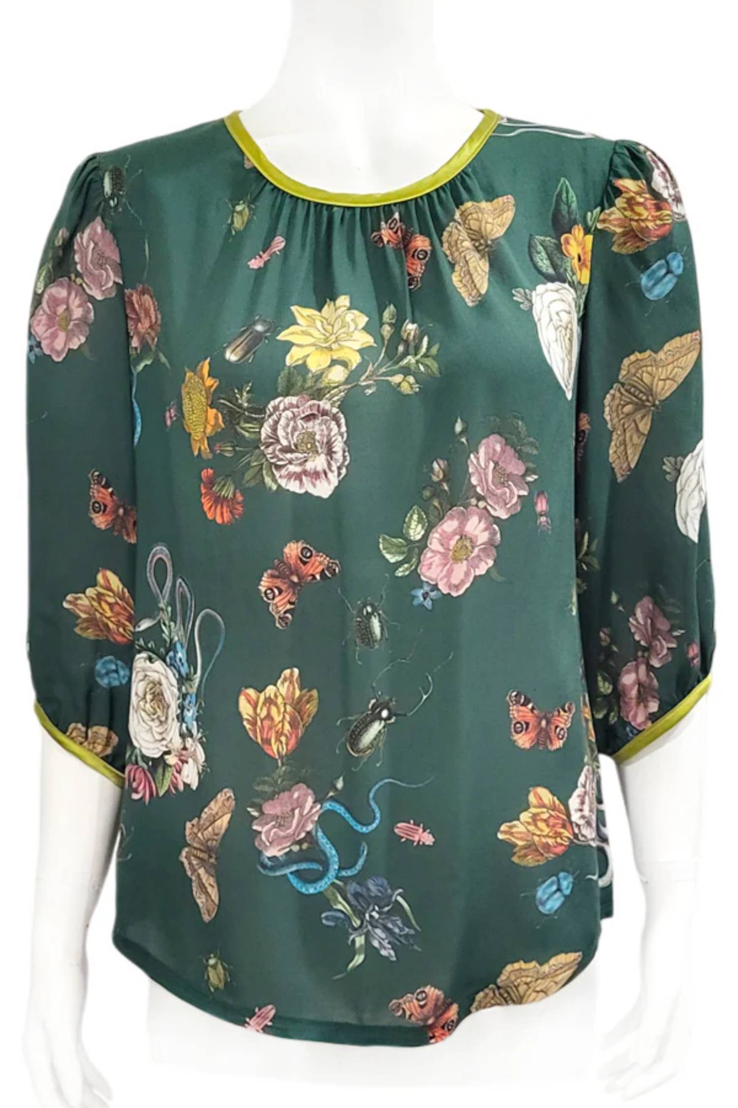 The Lydia Creeper Blouse by Mandala in Forest is shown in front of a white background. It features a vintage floral print with snakes and insects, with a jewel neck, puffed 3/4 sleeves, and a scooped hem. 