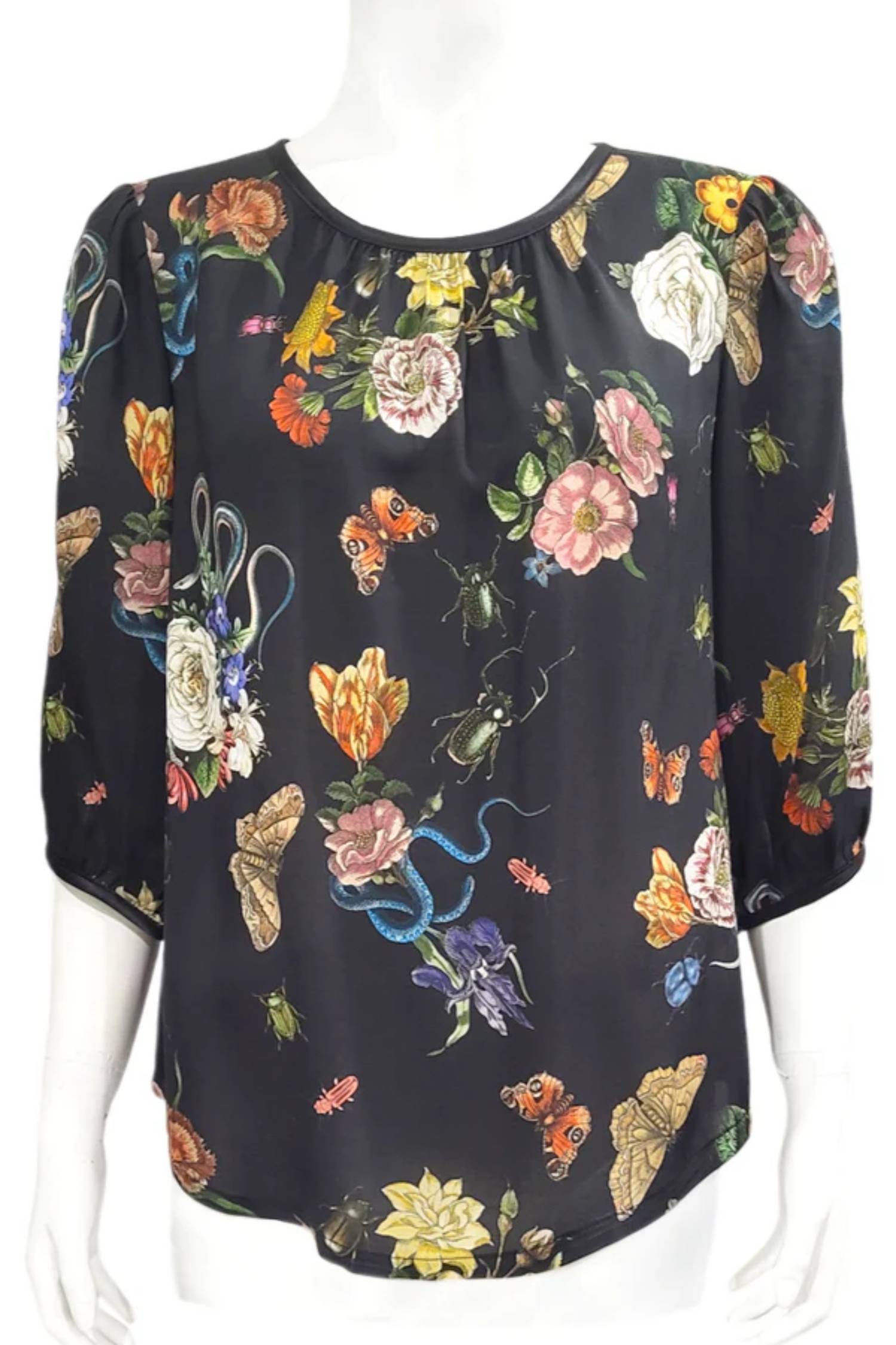 The Lydia Creeper Blouse by Mandala in Onyx is shown in front of a white background. It features a vintage floral print with snakes and insects, with a jewel neck, puffed 3/4 sleeves, and a scooped hem. 