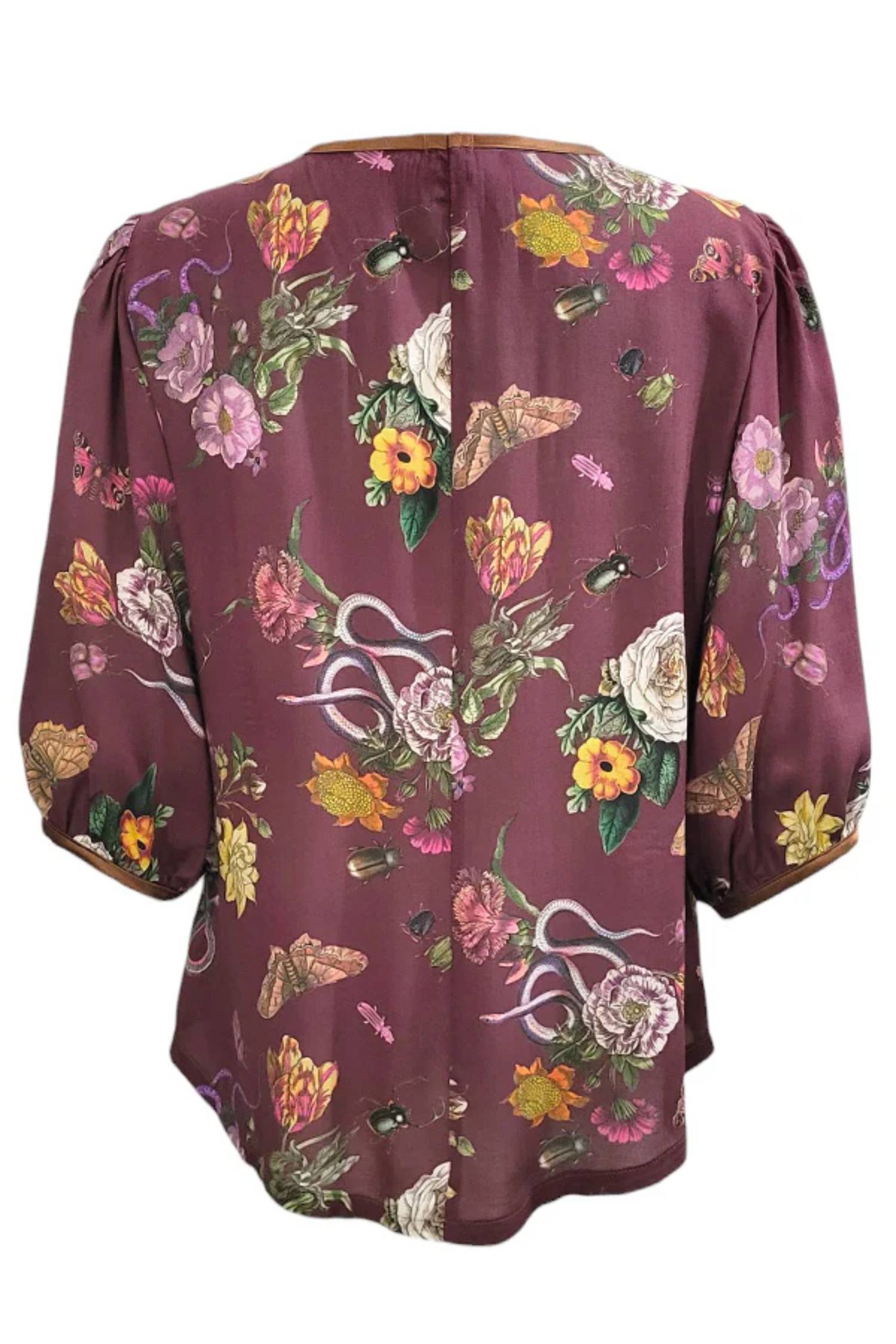 The back of the Lydia Creeper Blouse by Mandala in Oxblood is shown in front of a white background. It features a vintage floral print with snakes and insects, with a jewel neck, puffed 3/4 sleeves, and a scooped hem. 