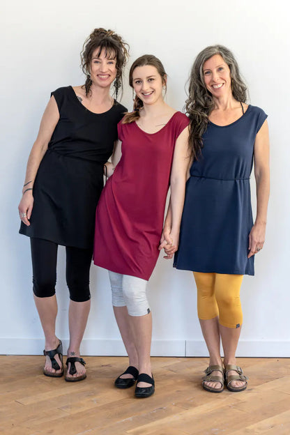 Three women wearing the Mariposa Dress by Marie C, a short sleeved short dress that's reversible back to front with printed yoke on one side, and an attached tie belt. The one in the centre is wearing it in Raspberry. 