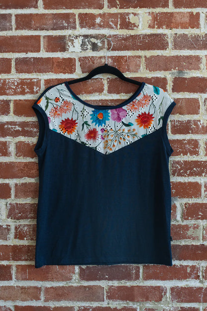 The Pepita Top from Marie C, a reversible t-shirt with a printed fabric yoke on one side, in Navy and White is shown hanging on a brick wall.