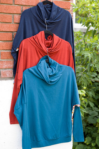 The Marie C Mimoso Top in Navy, Rust, and Teal is shown hanging in front of a brick wall
