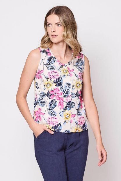3/4 view of a woman wearing the Marney Tank Top by Tangente in White Floral, with a round neck, full-length centre pleat, and darts at the bust. She is wearing it with navy pants and standing in front of a white background. 