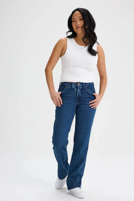 A woman wearing the Marianne Straight Leg Denim Pants by Message Factory, featuring a straight leg, a 31 inch inseam, and organic cotton fabric, with a white tank. She is standing in front of a white background. 