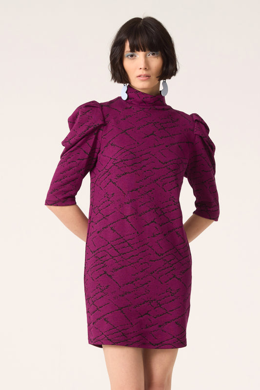 3/4 shot of a woman wearing the Nostalgia Dress by Cokluch in Magenta, standing in front of a white  background.