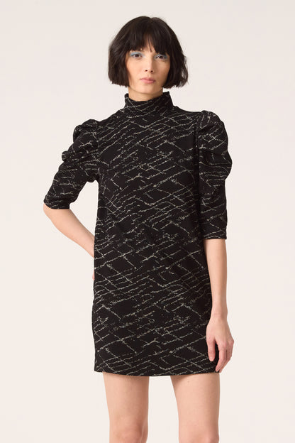 3/4 shot of a woman wearing the Nostalgia Dress by Cokluch in Black, standing in front of a white  background.