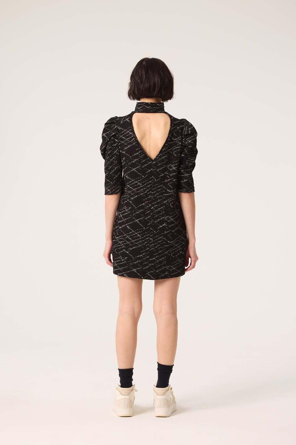 Back view of a woman wearing the Nostalgia Dress by Cokluch in Black, standing in front of a white  background.