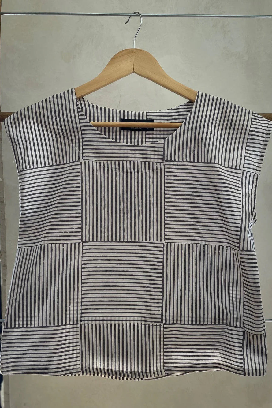 The Sandrigo Top from Kazak in Ori Cream print, a cotton top with short extended sleeves and a wide round neck, is shown on a wooden hanger against a grey background. 